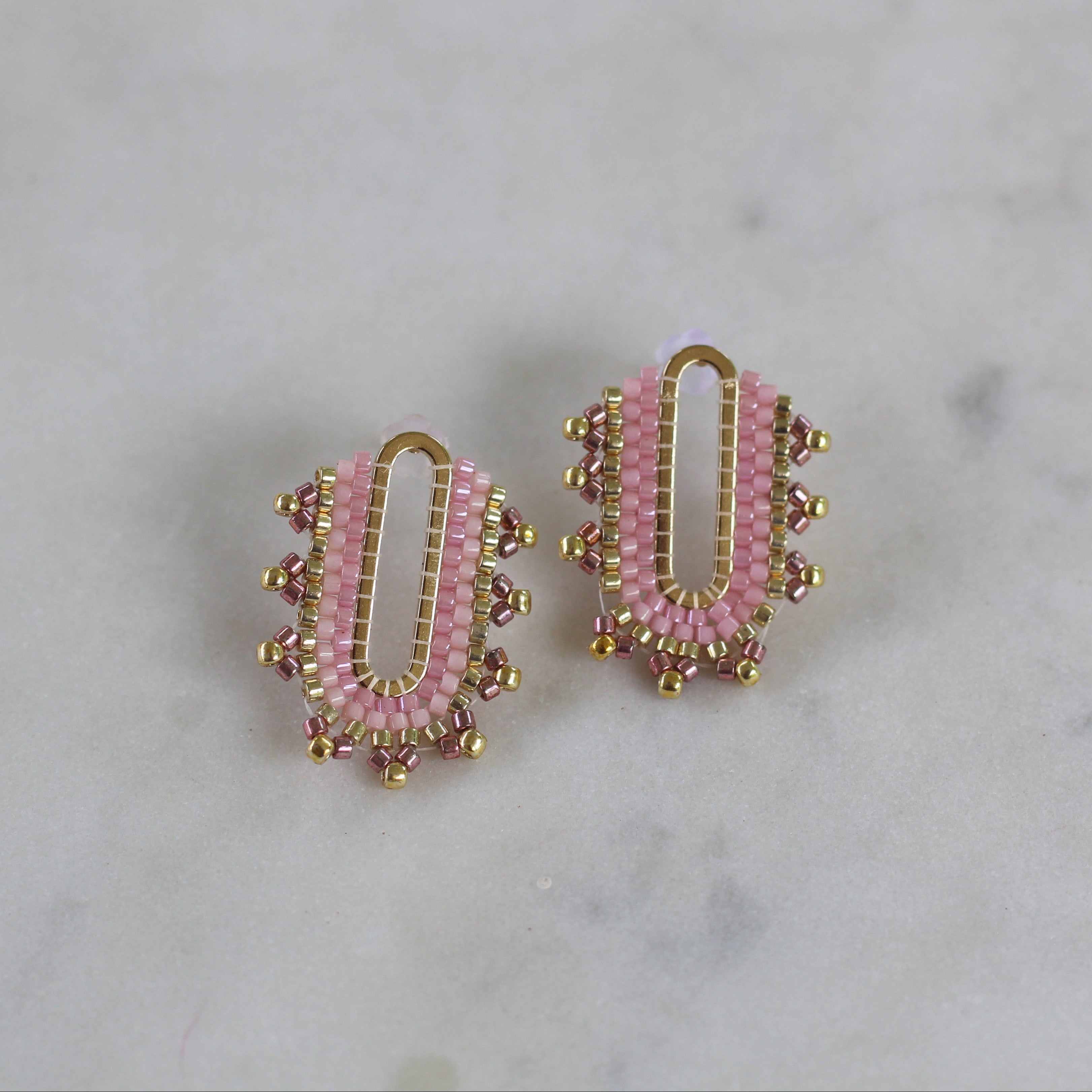 Pair of pink beaded earrings with gold accents on a marble background